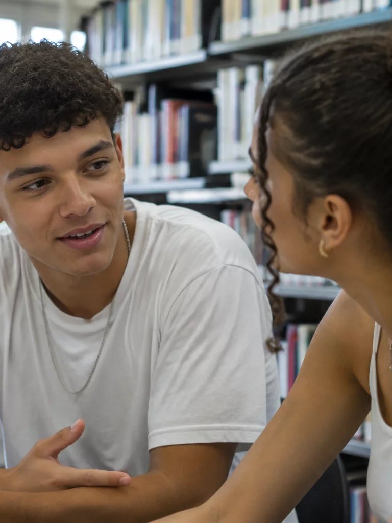 Duas participantes conversando de pé no corredor entre prateleiras de livros