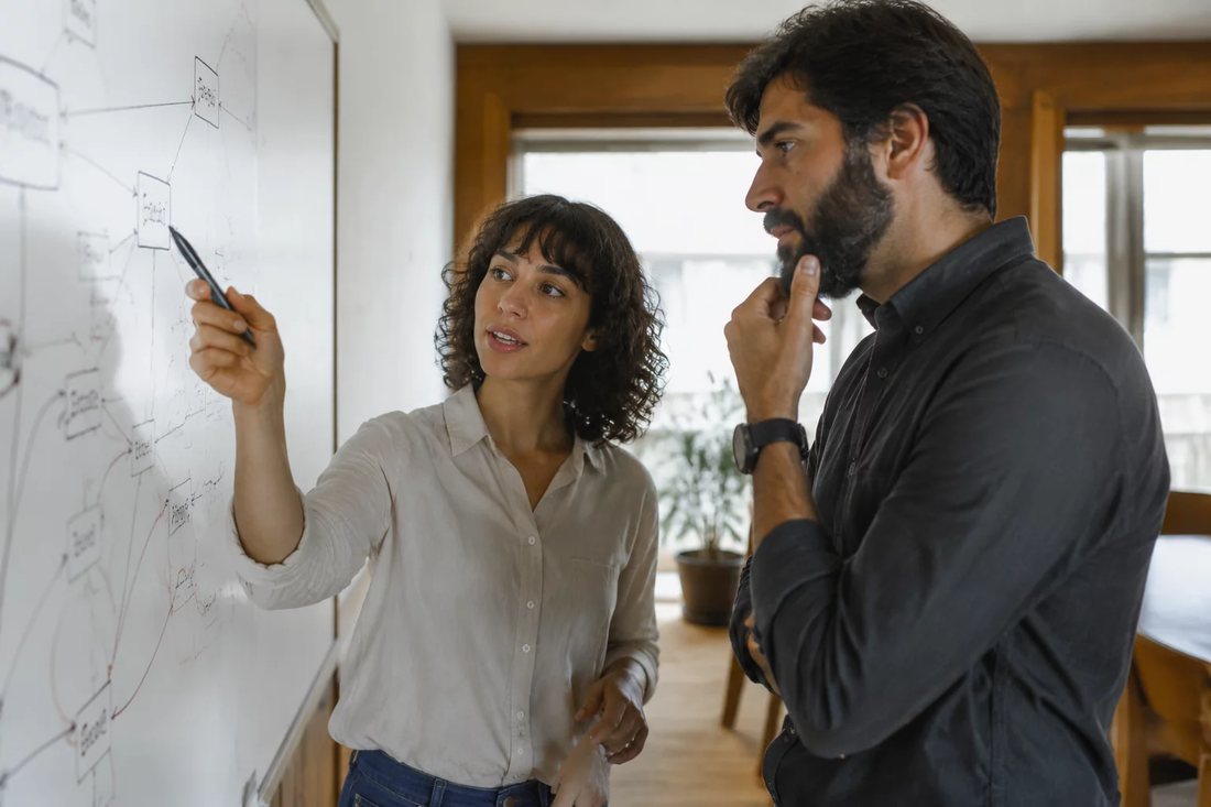 Duas pessoas diante de um quadro branco com a armação de um argumento rabiscada